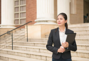 Business woman standing in front of court and holding legal documents waiting for customers ready to handle case.