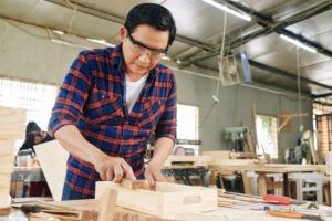 Serious mature carpenter in goggles polishing drawer with wooden block